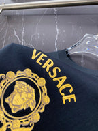 Black T-shirt close-up of gold Versace crest emblem and curved logo letters