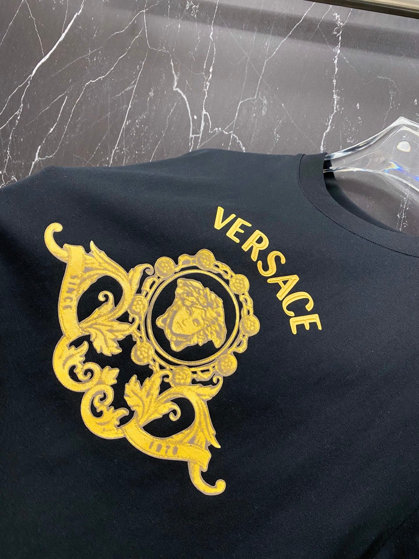 Black T-shirt close-up of gold Versace crest and VERSACE text across the chest