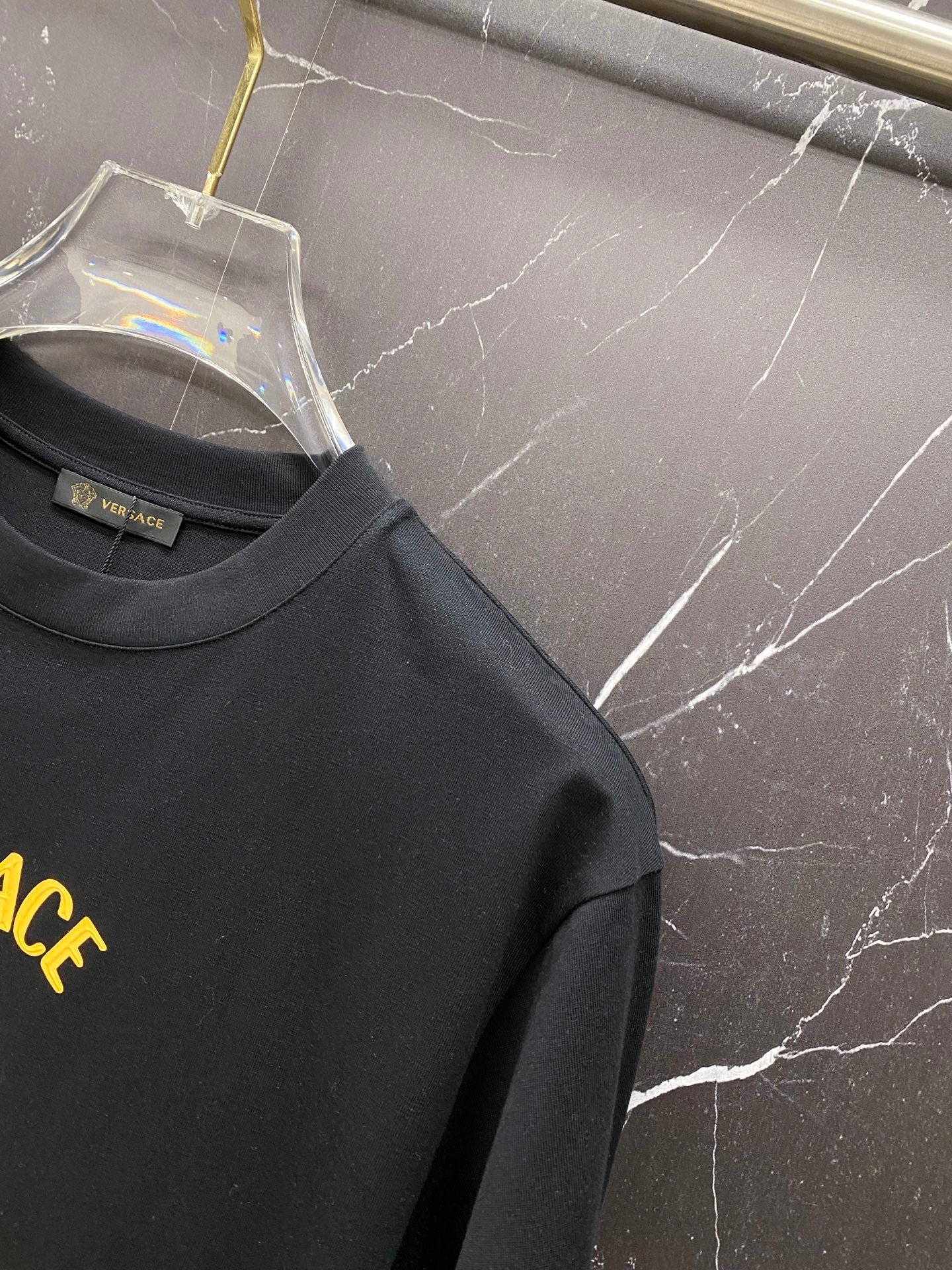 Black Versace T-shirt sleeve and partial yellow-gold logo.