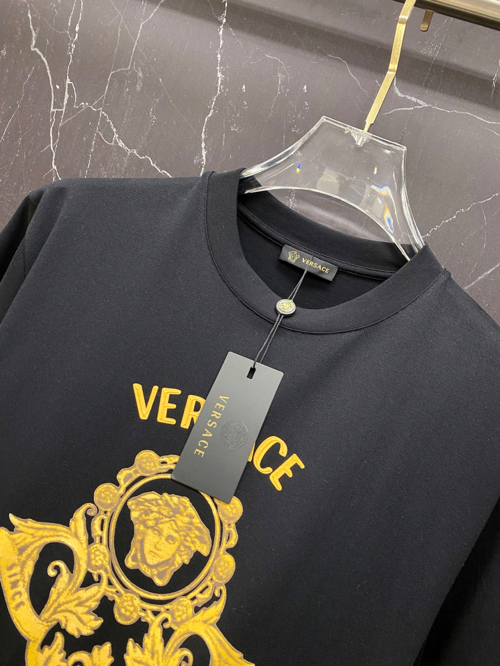 Black Versace T-shirt on hanger with brand tag and gold logo.