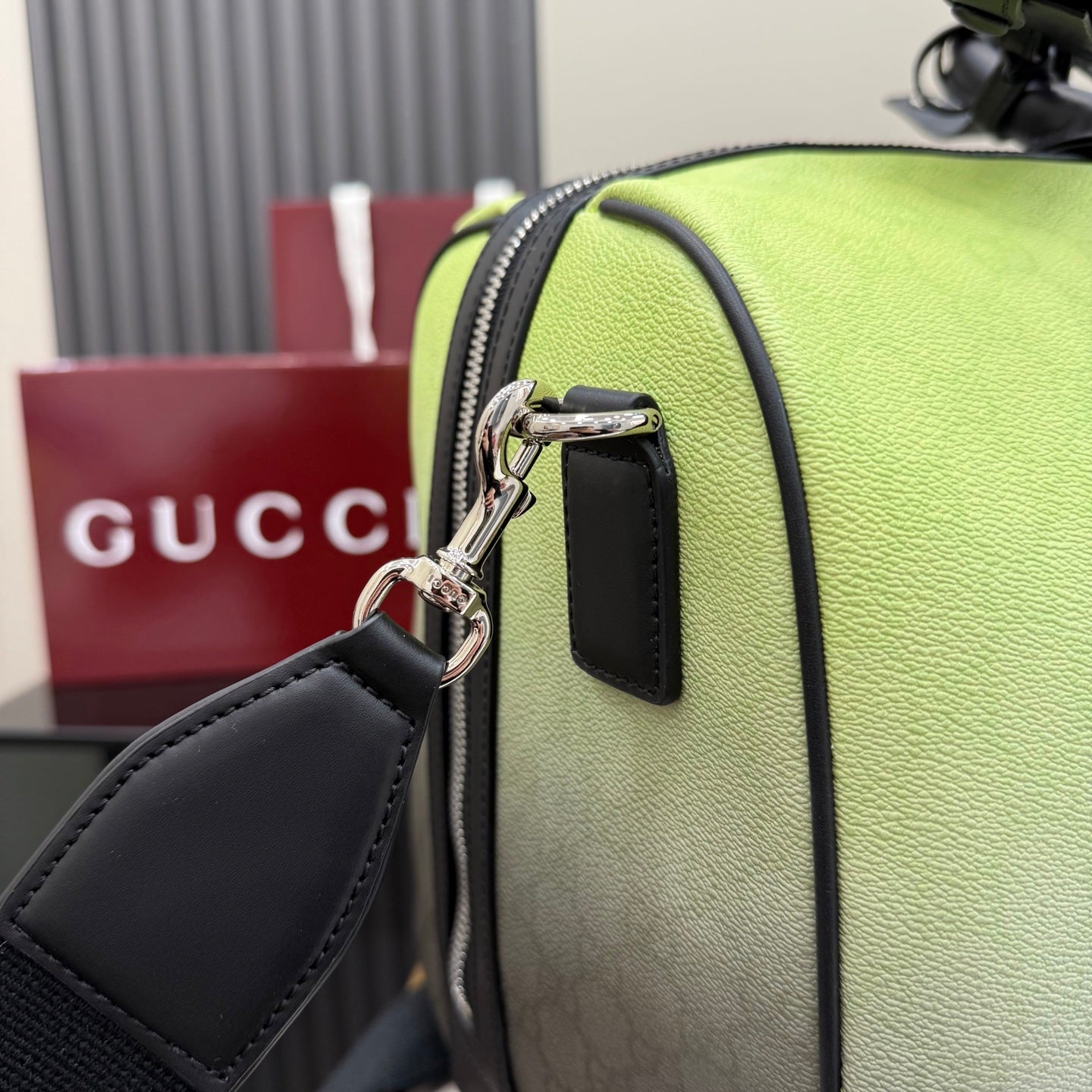 Green duffel bag close-up with silver hardware, black strap tab, and top zip opening
