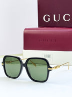 Black square sunglasses with green-tinted lenses and gold-tone temple detail