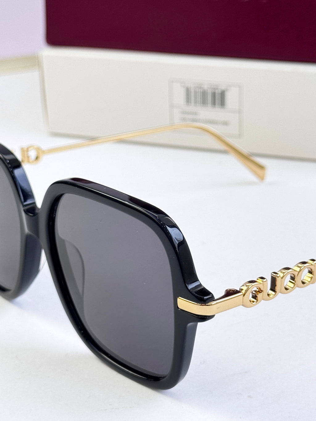 Close-up of black square sunglasses with gold-tone logo and clear nose pads