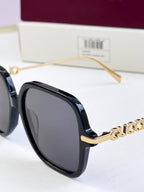 Close-up of black square sunglasses with gold-tone logo and clear nose pads