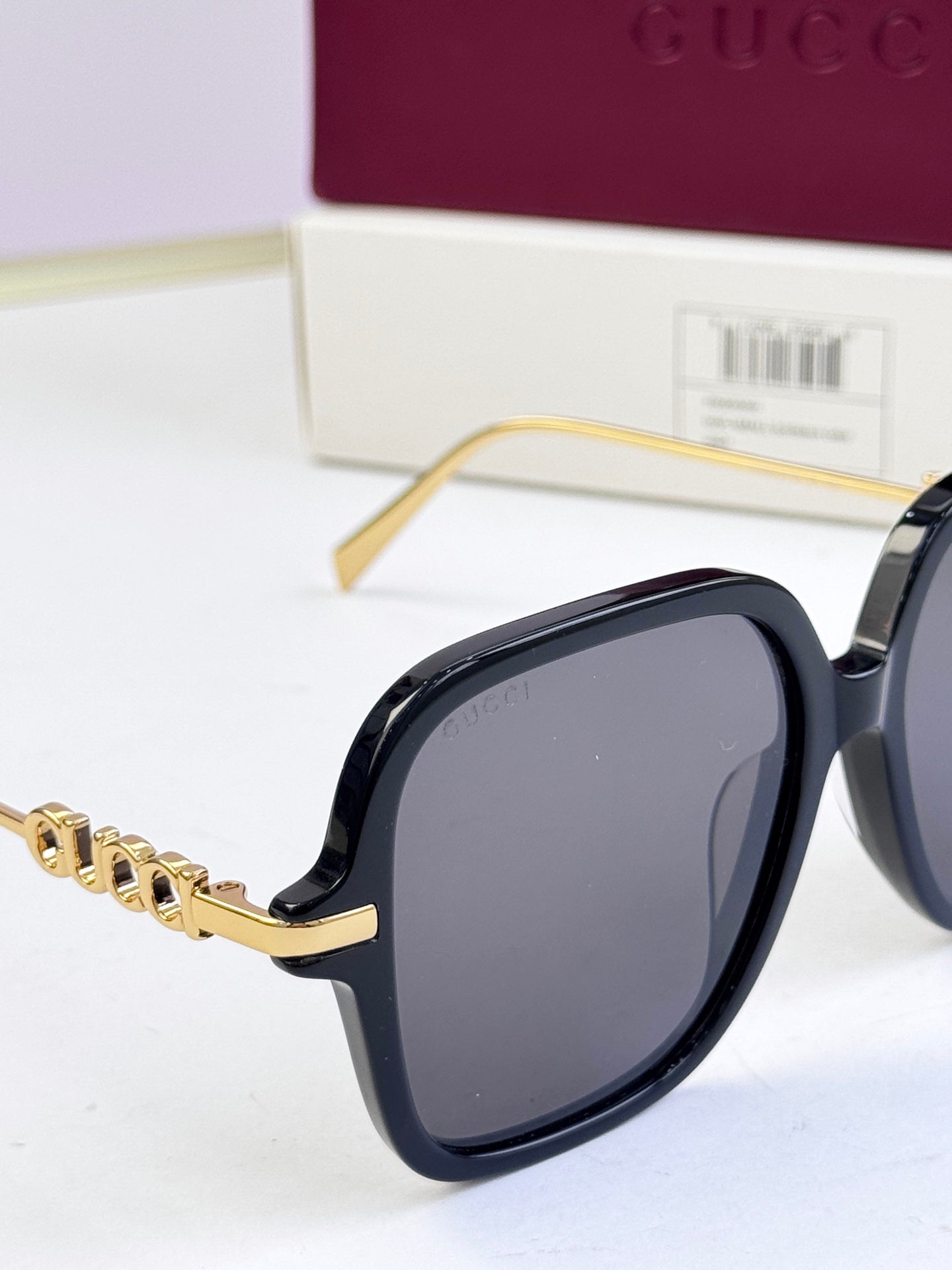 Close-up of black square sunglasses with gold-tone logo on temple