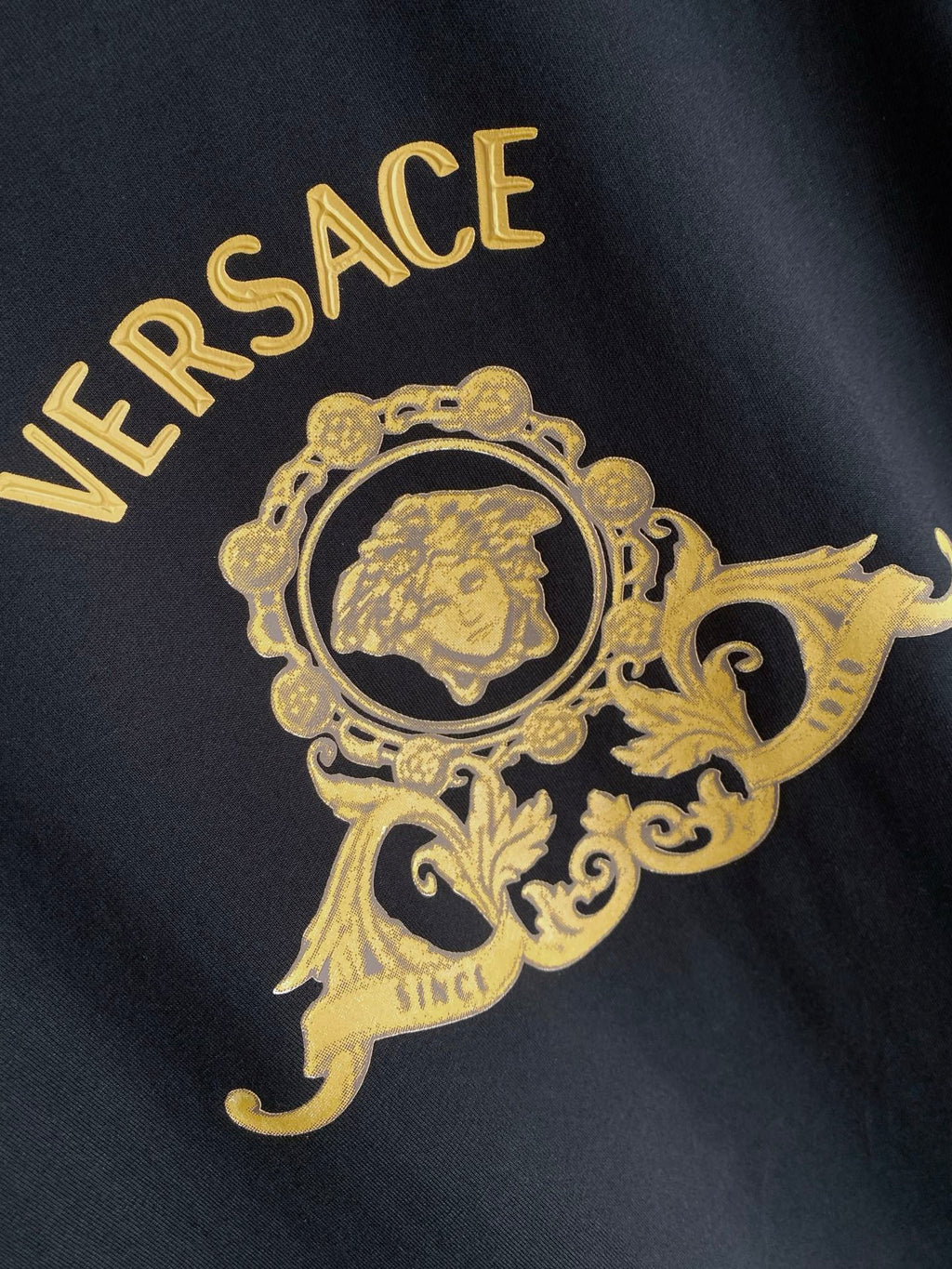 Versace T-shirt graphic close-up: gold crown crest and VERSACE text