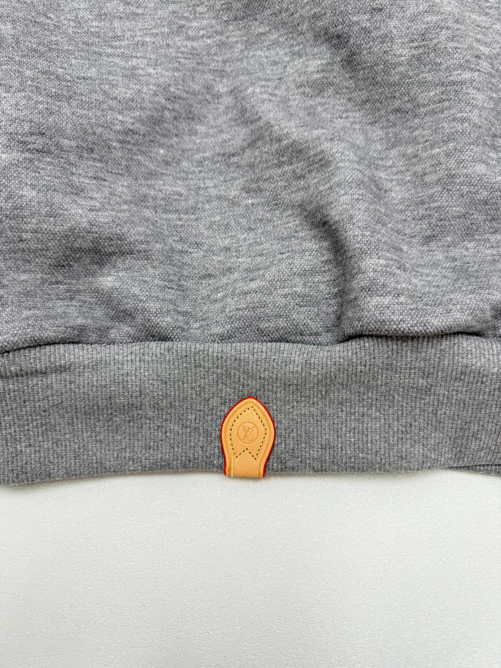 Gray hoodie hem with small orange leather-look logo patch at the center