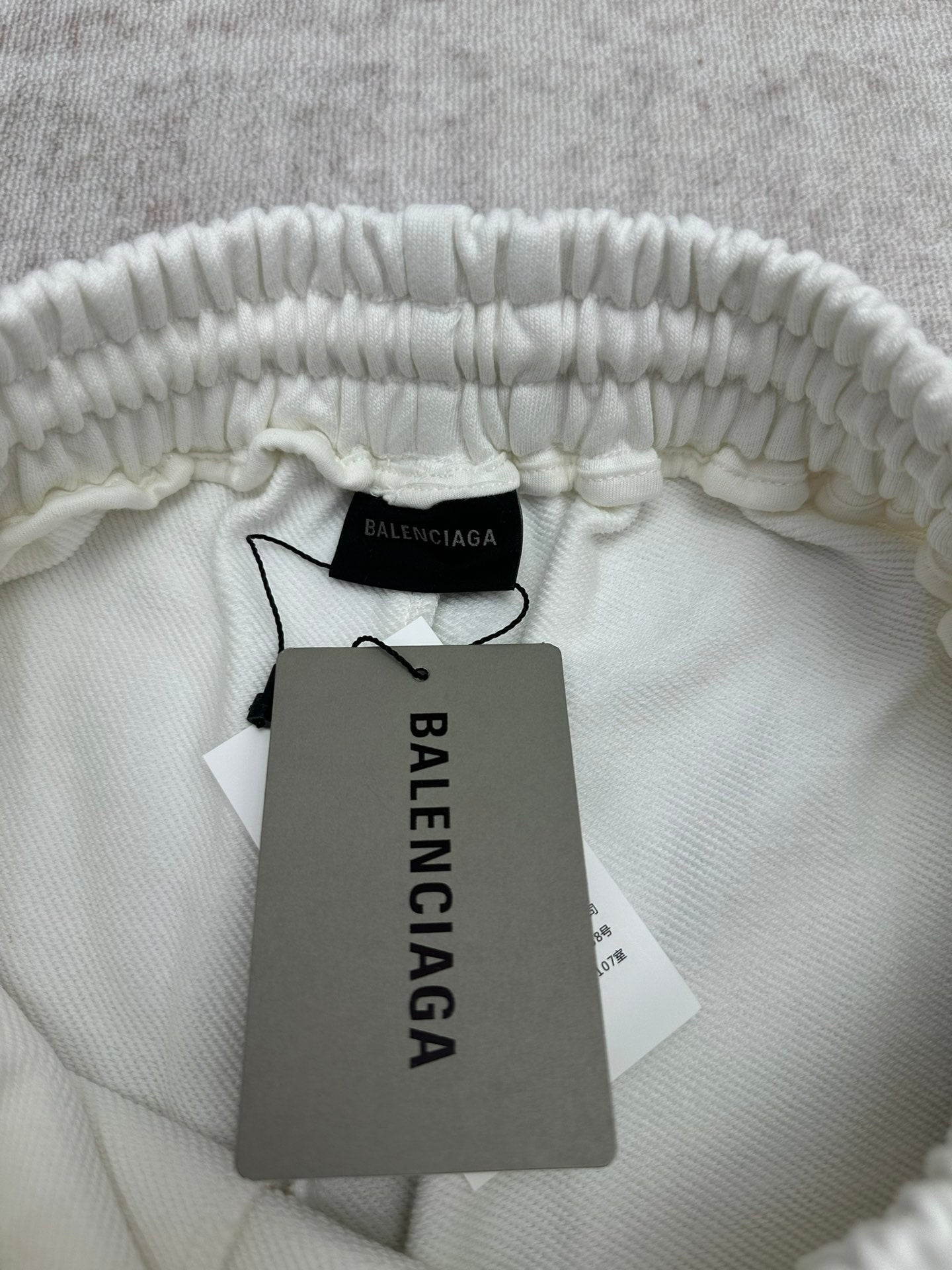 White pants interior waistband with Balenciaga label and hanging price tag, close-up.