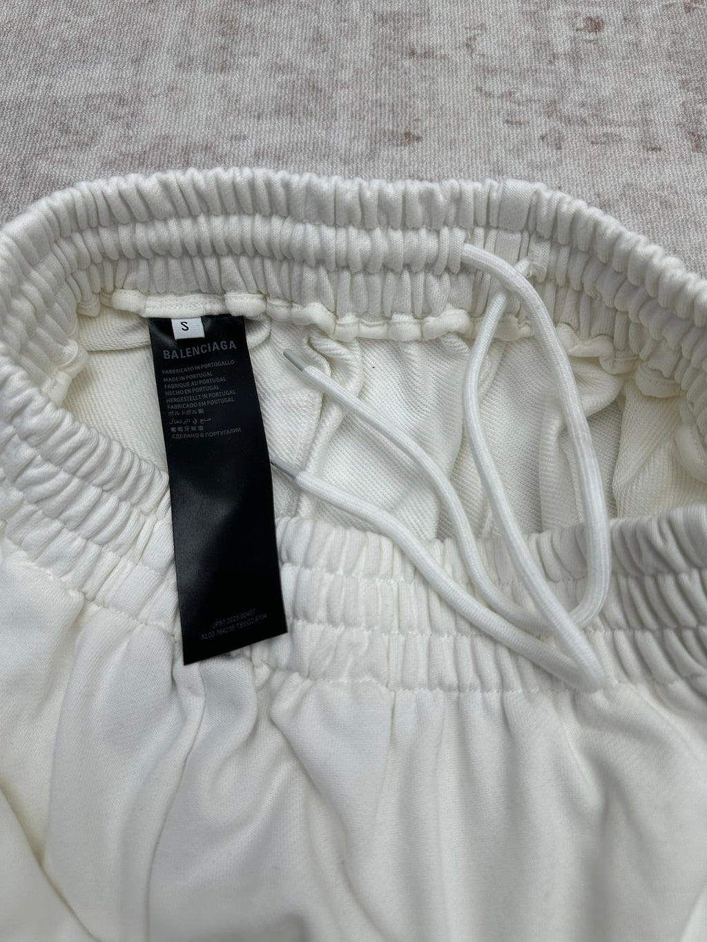 White pants waistband with interior drawstring and size tag, close-up.