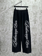 Black Balenciaga track pants with elastic waistband and large white script logo