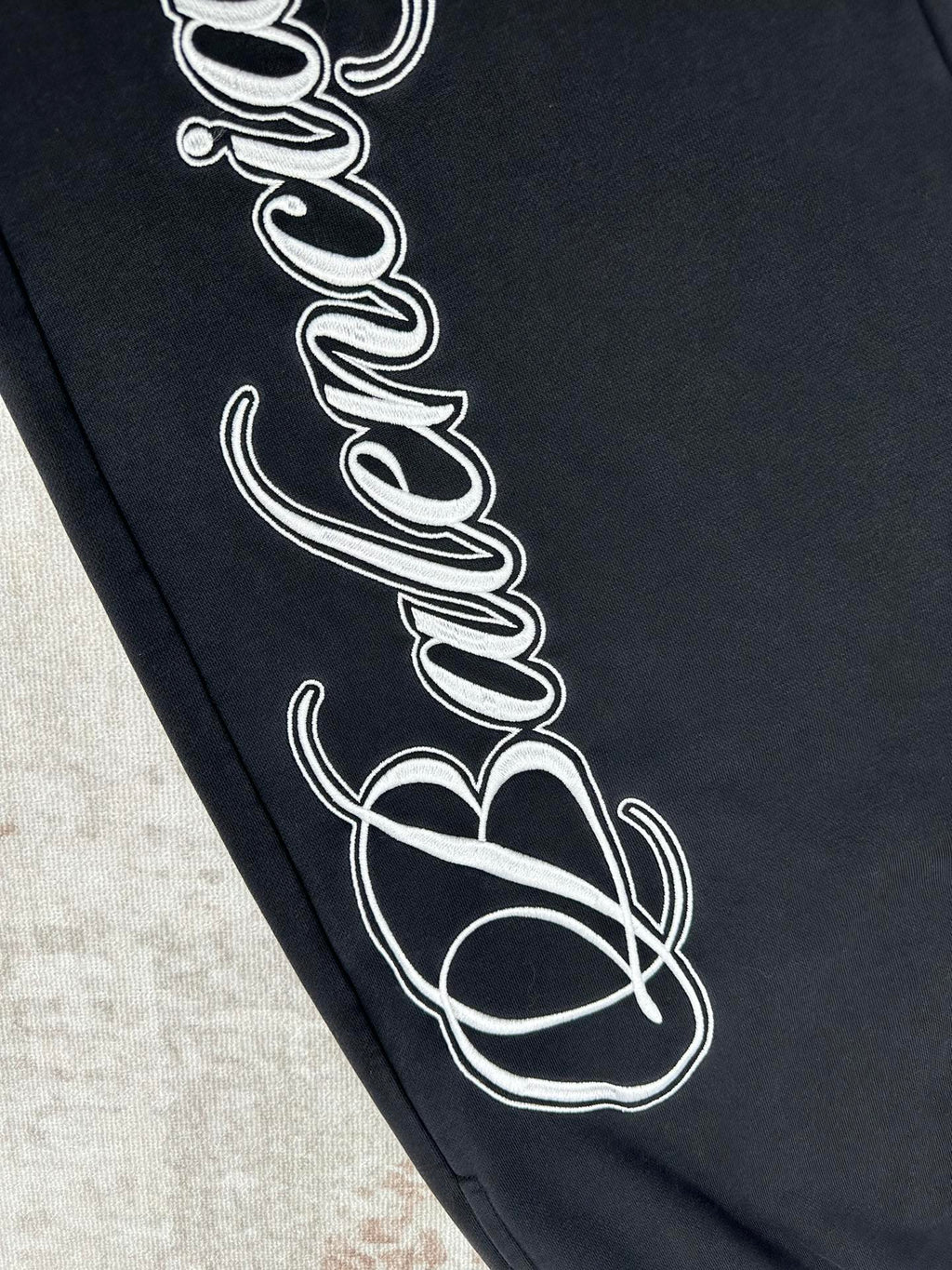 Black pants fabric close-up with white outlined script print on leg