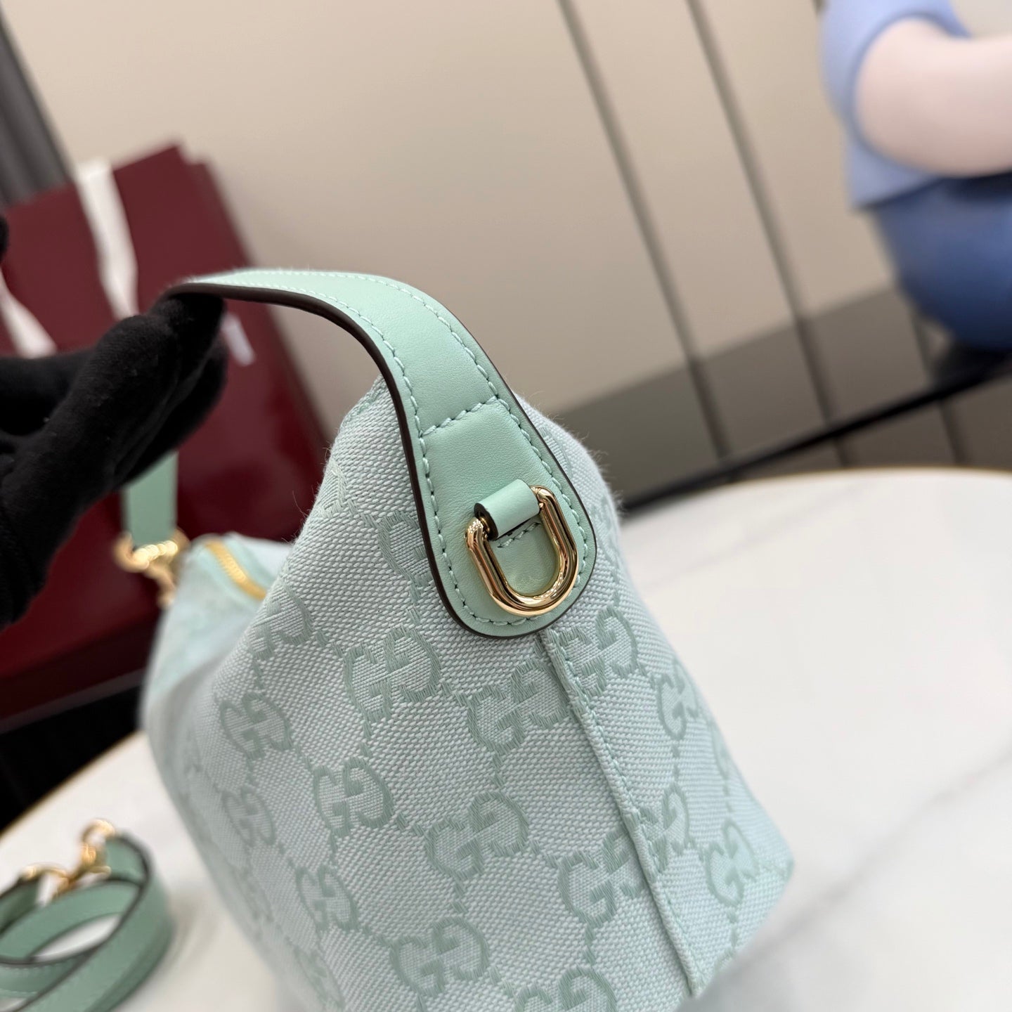 Small handbag with light teal leather handle tab, gold-tone clasp, monogram fabric.