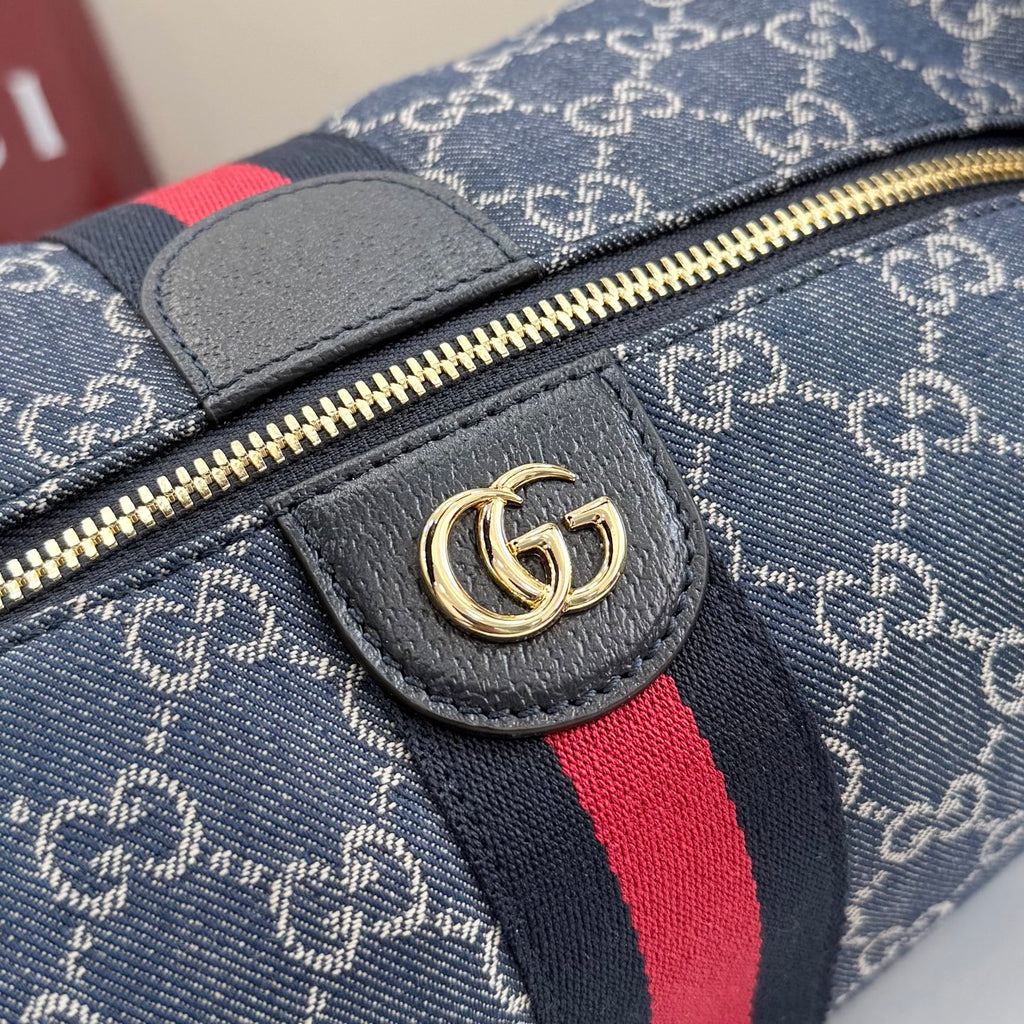 Gucci GG canvas bag close-up: navy fabric, gray leather tab, red stripe, gold zipper pull.