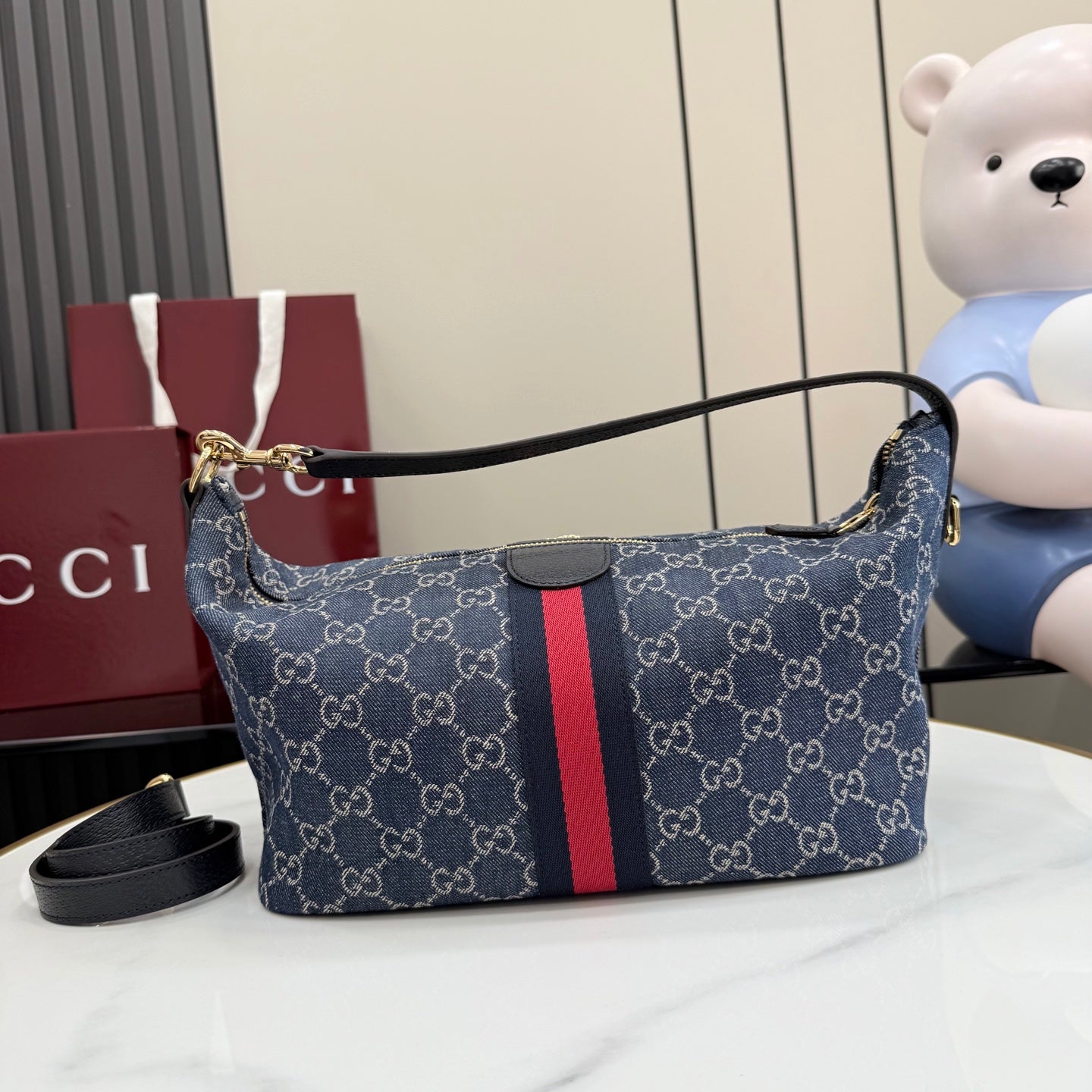 Gucci GG canvas shoulder bag with navy monogram print, red stripe, and top zipper closure.