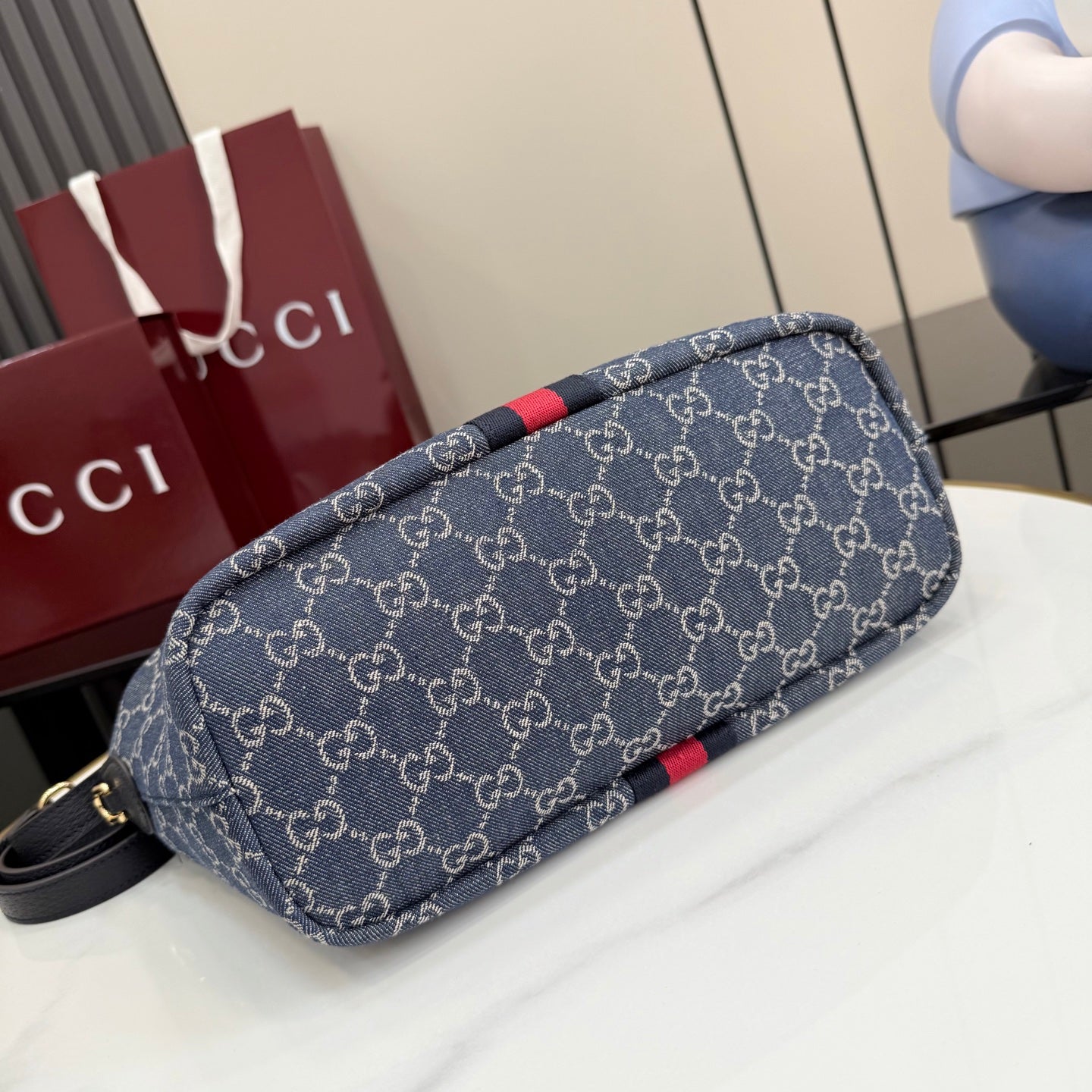 Gucci GG canvas shoulder bag laid on its side, navy monogram with red stripe trim.