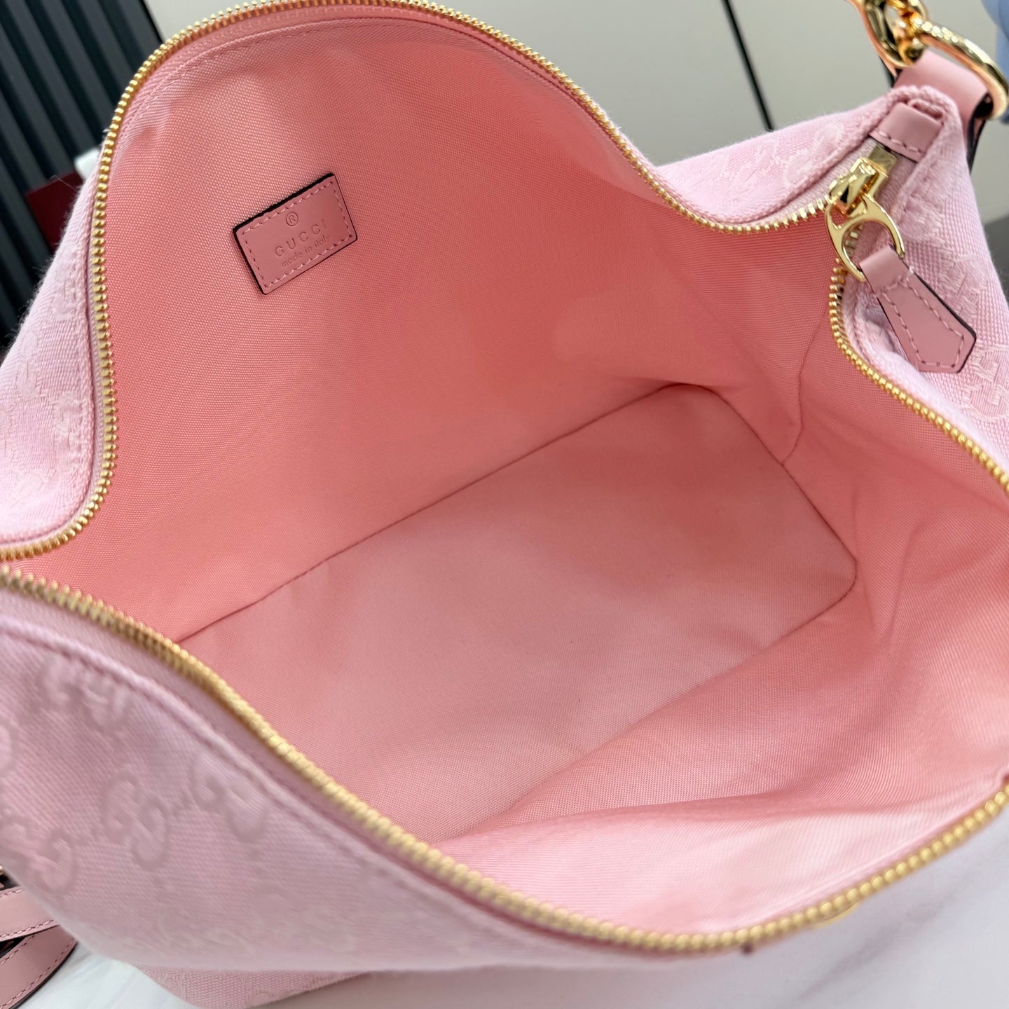 Pink interior of a zip-top shoulder bag with smooth lining and small logo label.