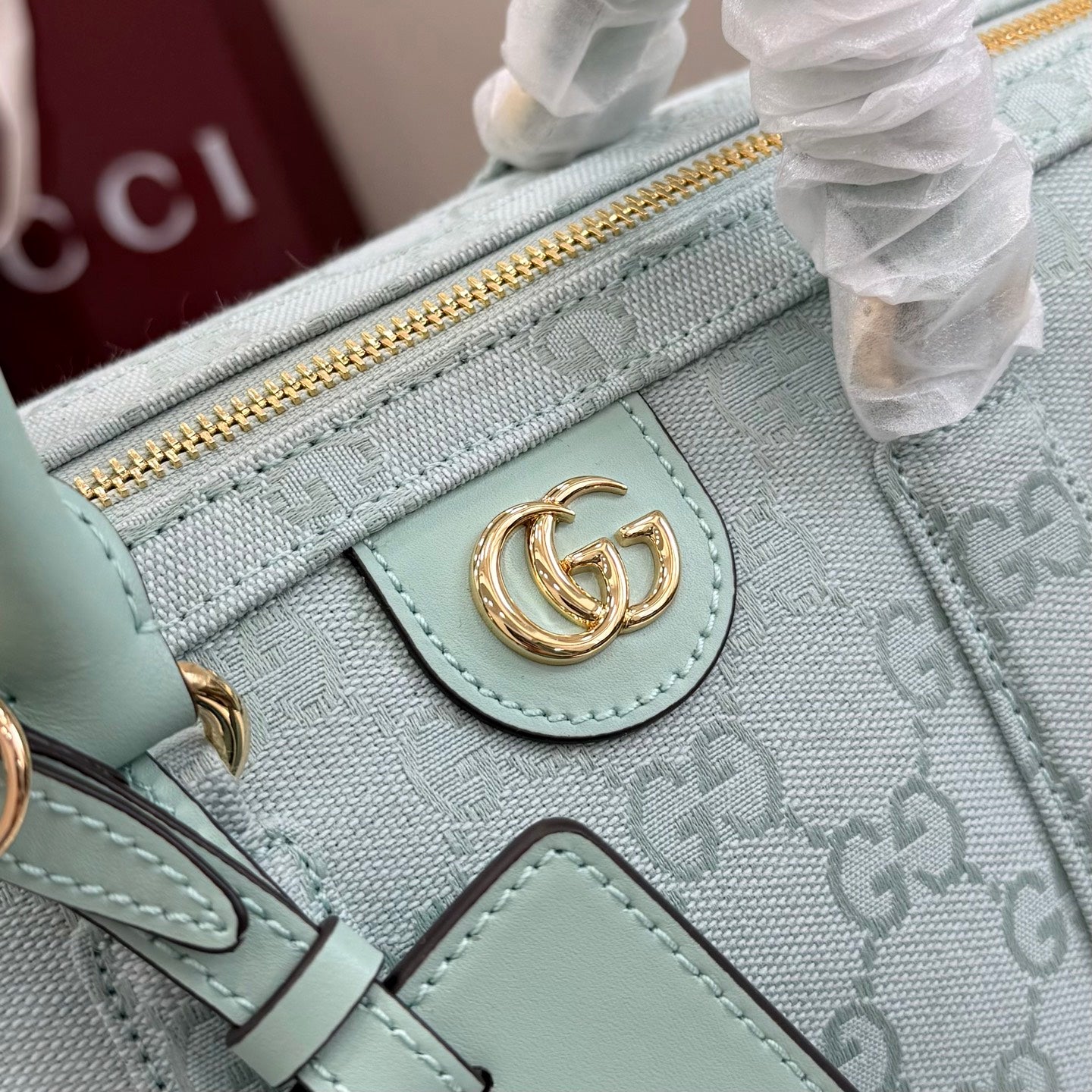 Mint leather tab detail on GG-pattern handbag with gold-tone clasp and zip pocket edge.