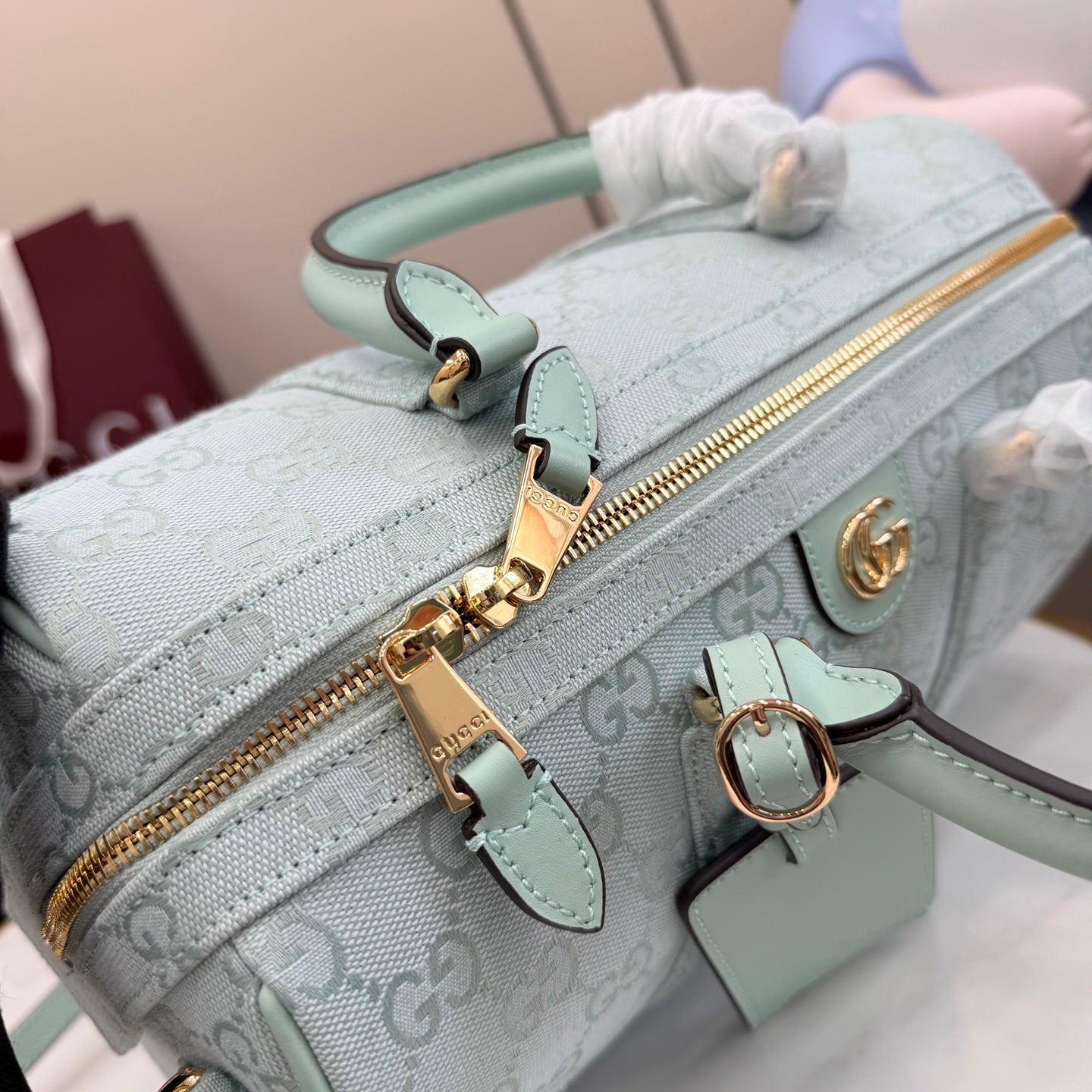 Mint GG-pattern handbag close-up of gold zipper, clasp hardware, and key fob charm.