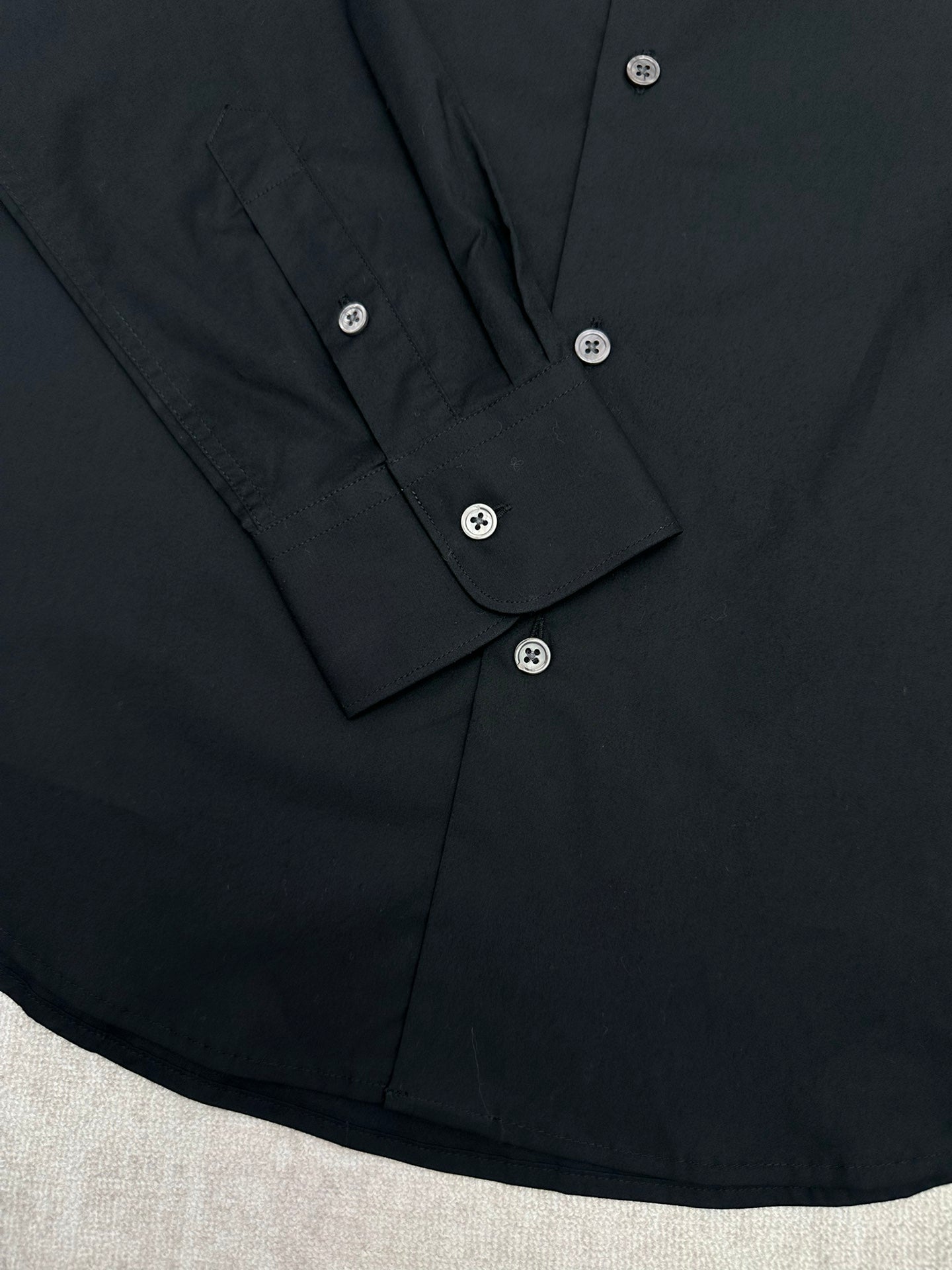 Black long-sleeve shirt button placket with folded cuffs and white buttons