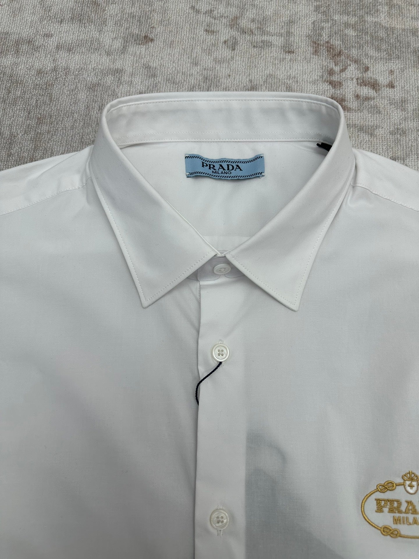 White dress shirt collar close-up with gold Prada crest and button