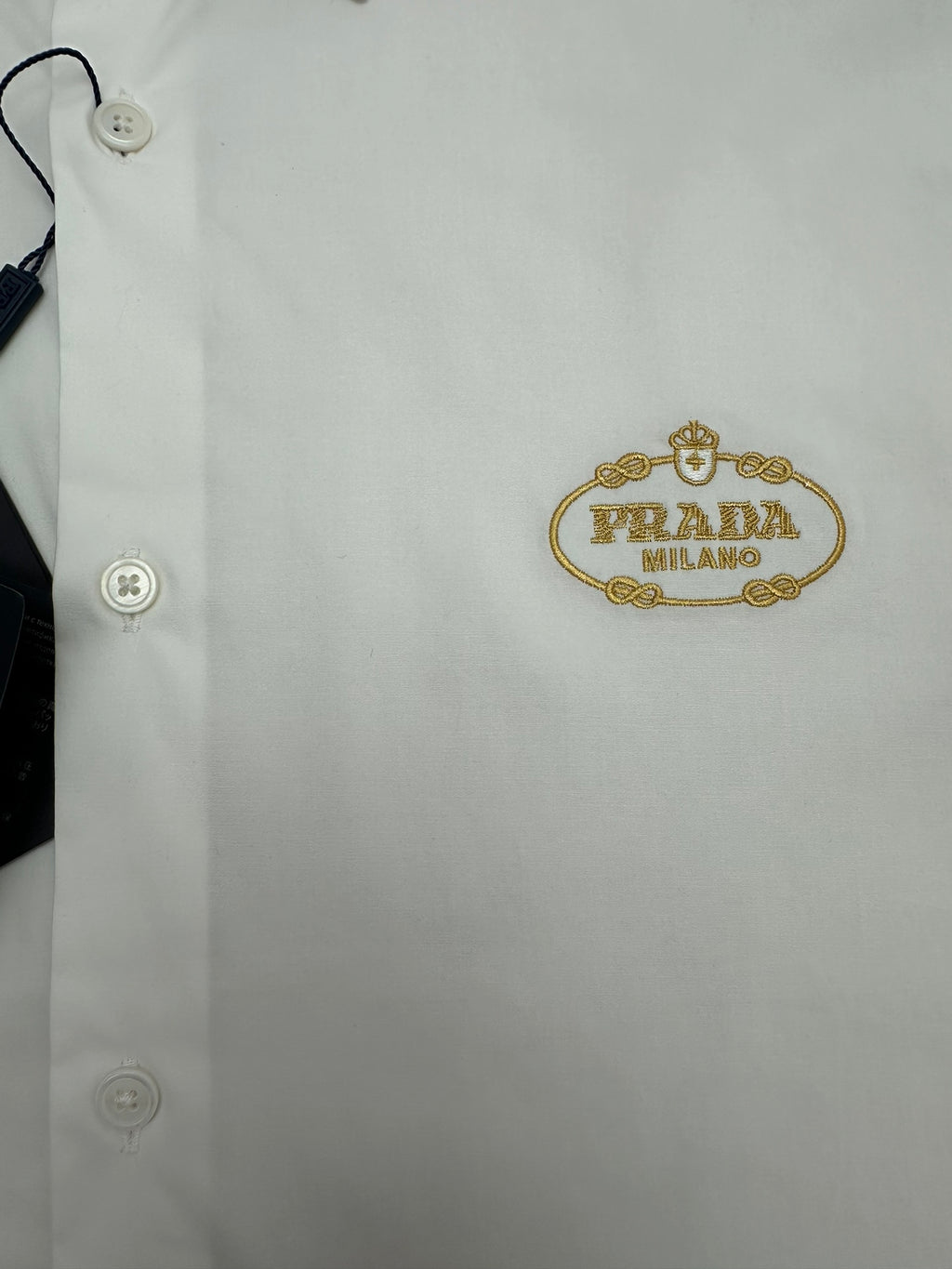 Prada long-sleeve button-up shirt detail, white fabric with gold logo patch