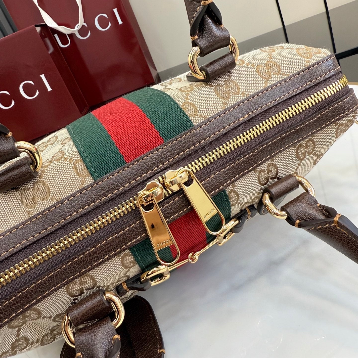Gucci canvas wristlet close-up with gold zipper pull and brown leather trim over web stripe