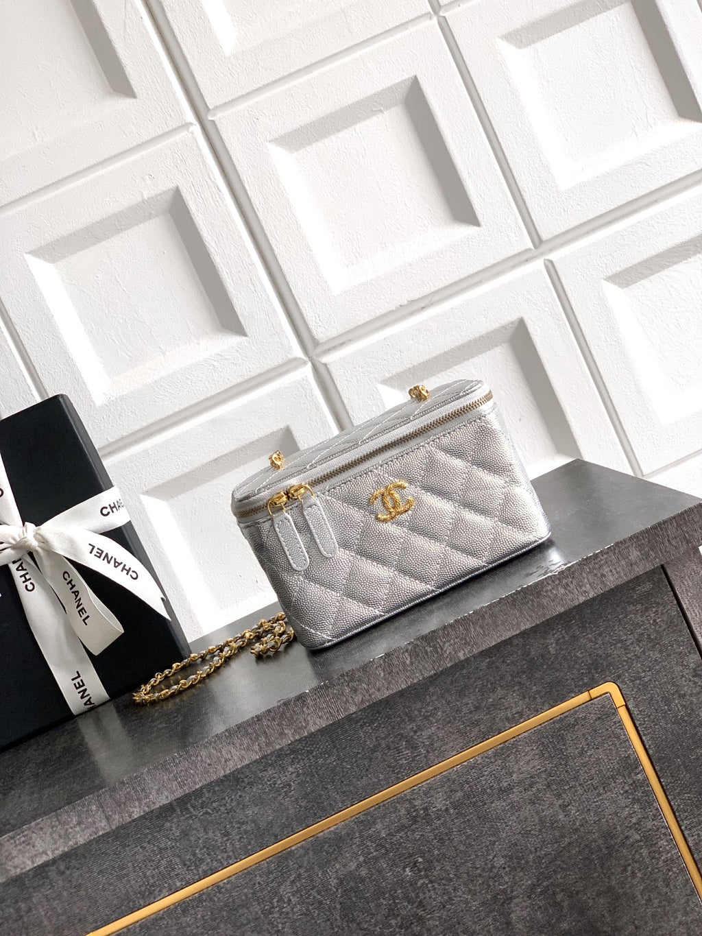 Light gray quilted Chanel bag with gold-tone chain strap and zip closure.
