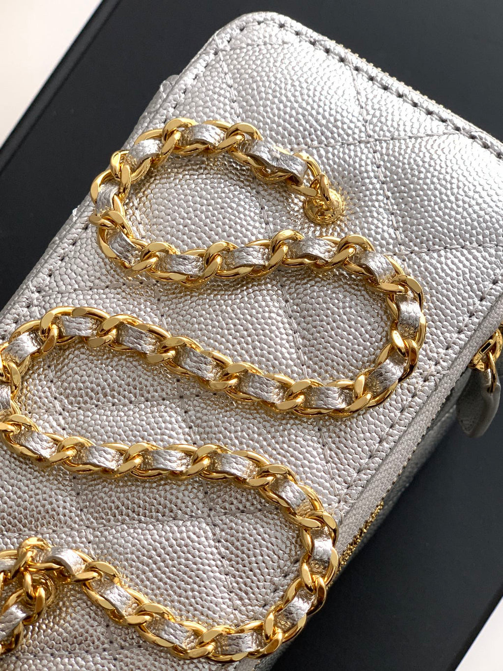 Light gray Chanel bag close-up of gold-tone chain strap on quilted leather.