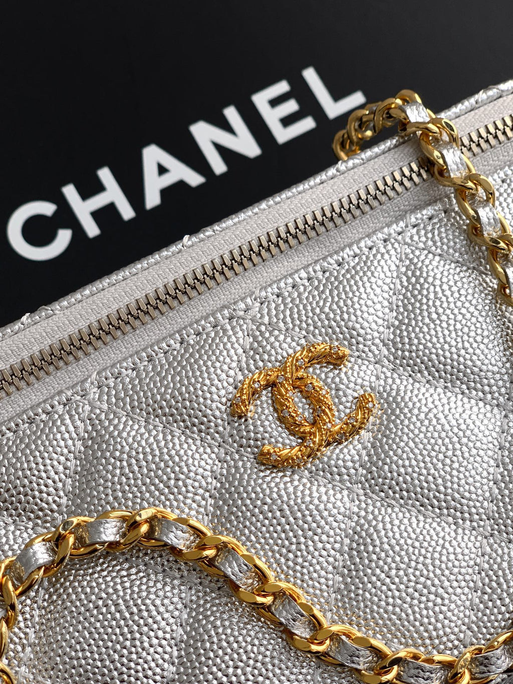 Light gray Chanel bag close-up of zip pull and CC logo on textured fabric.