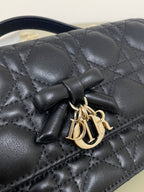 Dior quilted leather bag front with black bow and gold-tone logo clasp, dark navy