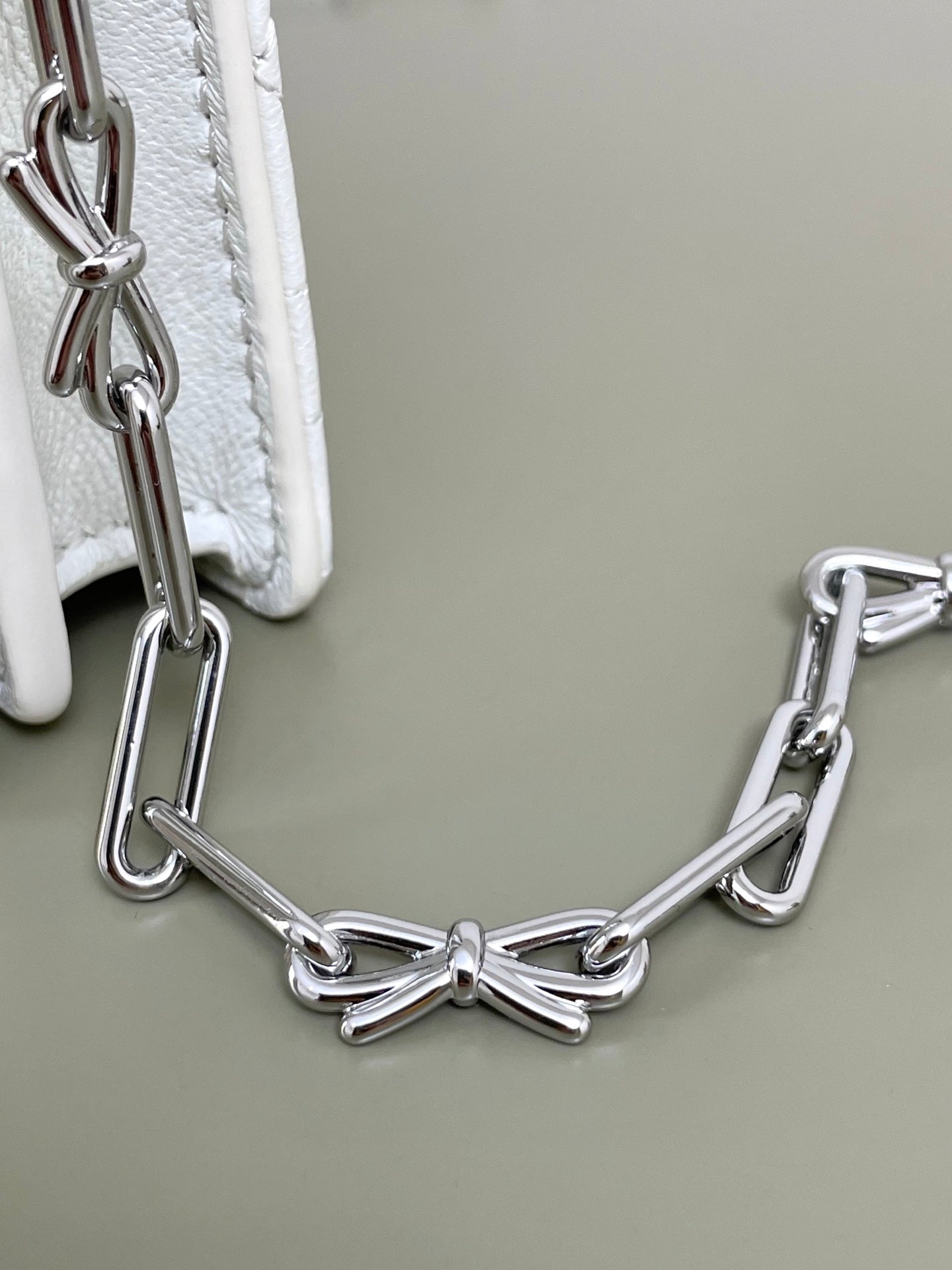 Silver chain handle attached to white quilted Dior bag