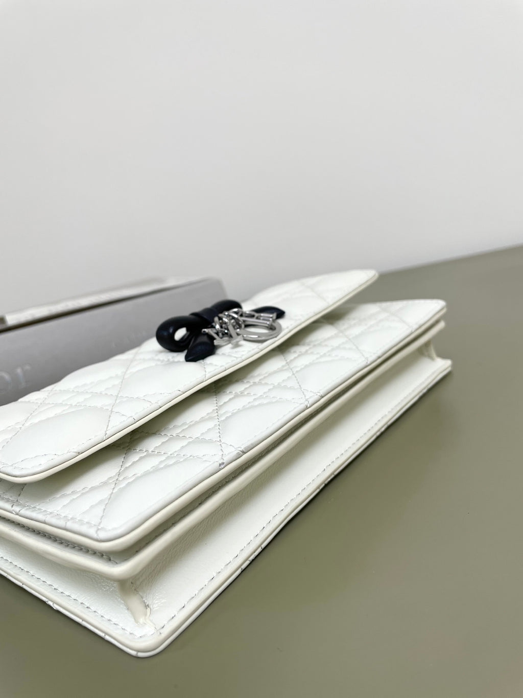 White flap bag with black bow clasp and silver chain, shown at side angle