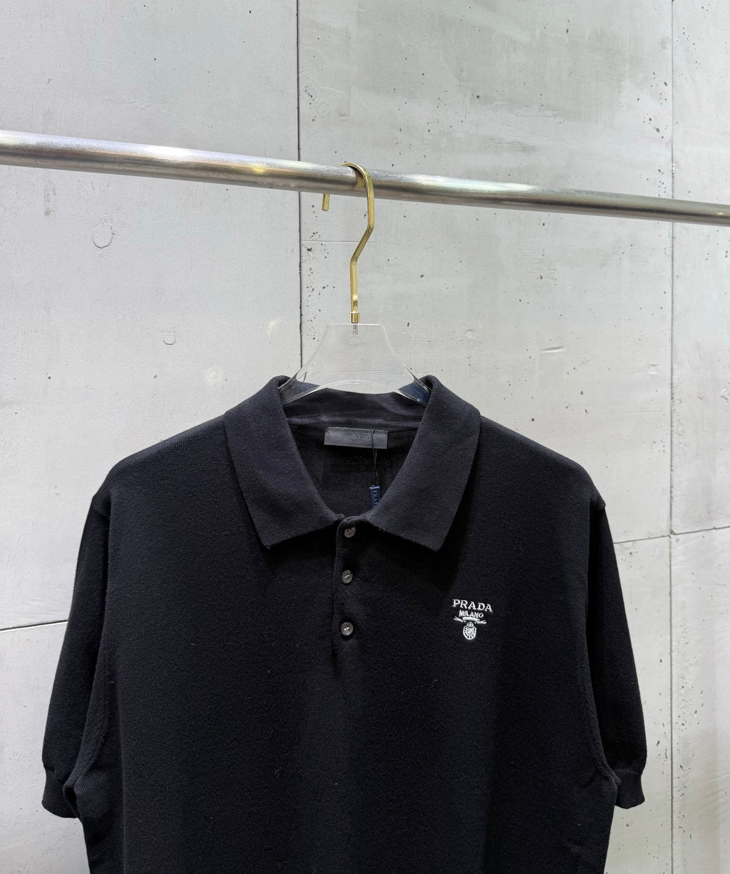 Black polo shirt with dark collar, button placket, and small chest logo