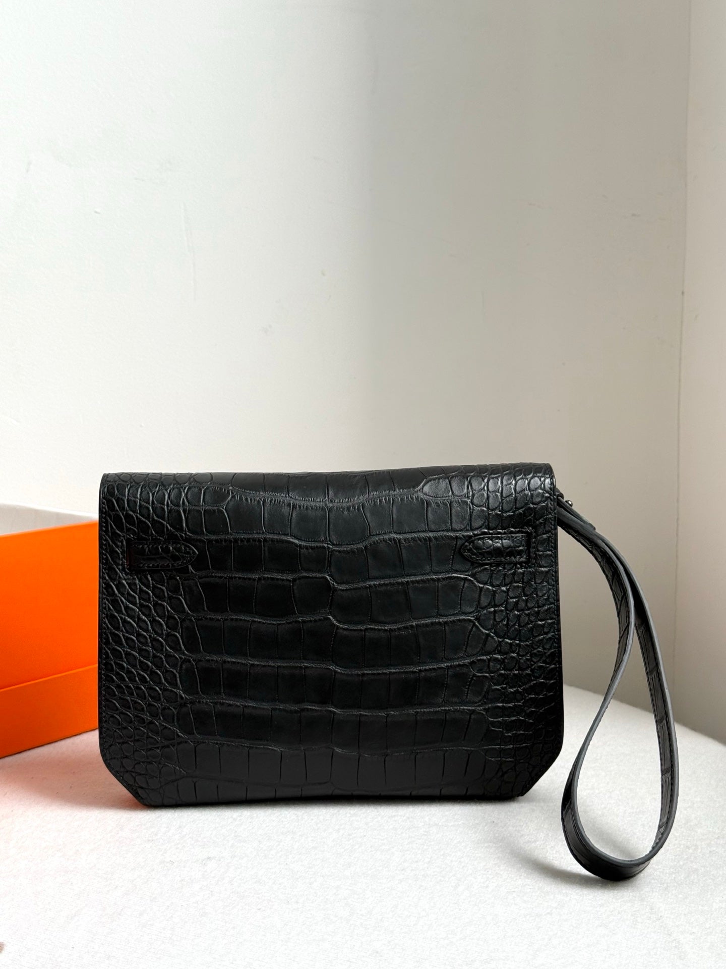 Hermes bag with dark croc-embossed finish, front flap, and attached wrist strap