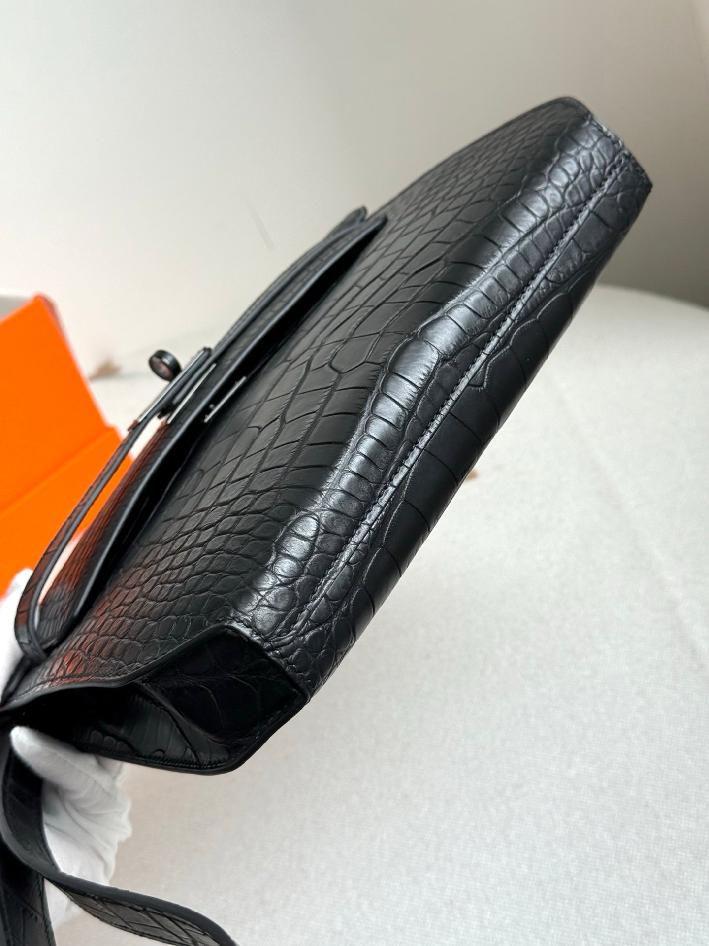Hermes bag side profile in dark crocodile-embossed leather with strap and open flap edge