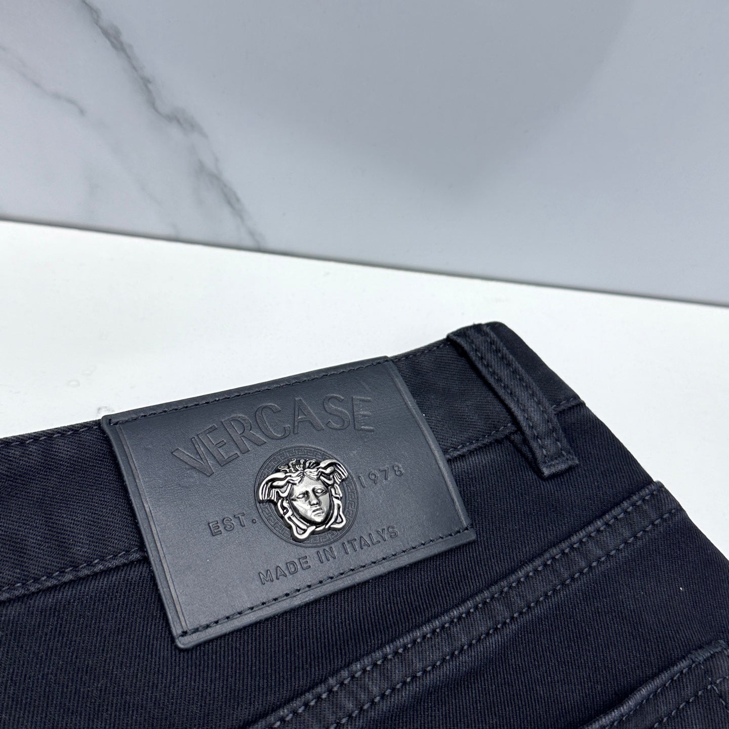 Versace dark blue jeans close-up of embossed leather logo patch on waistband
