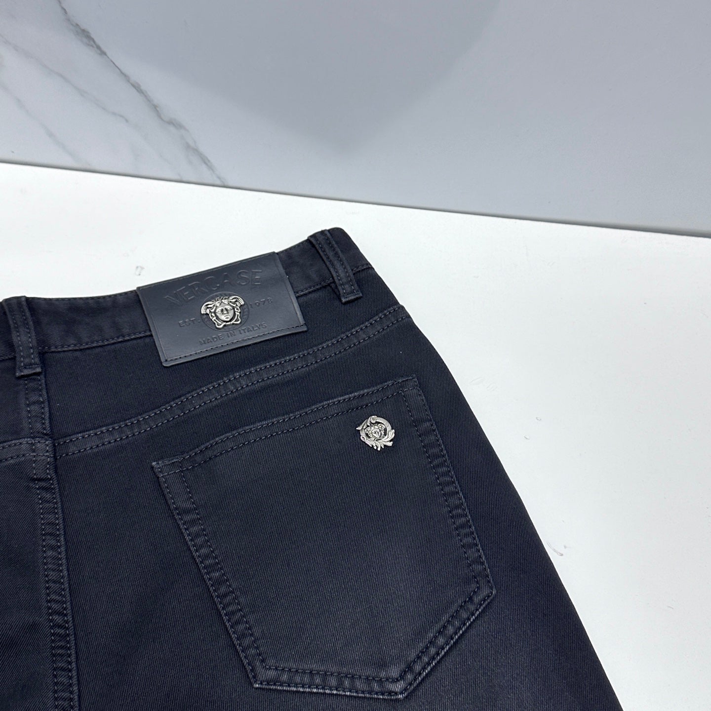 Versace dark blue denim jeans angled close-up of front pocket and logo patch
