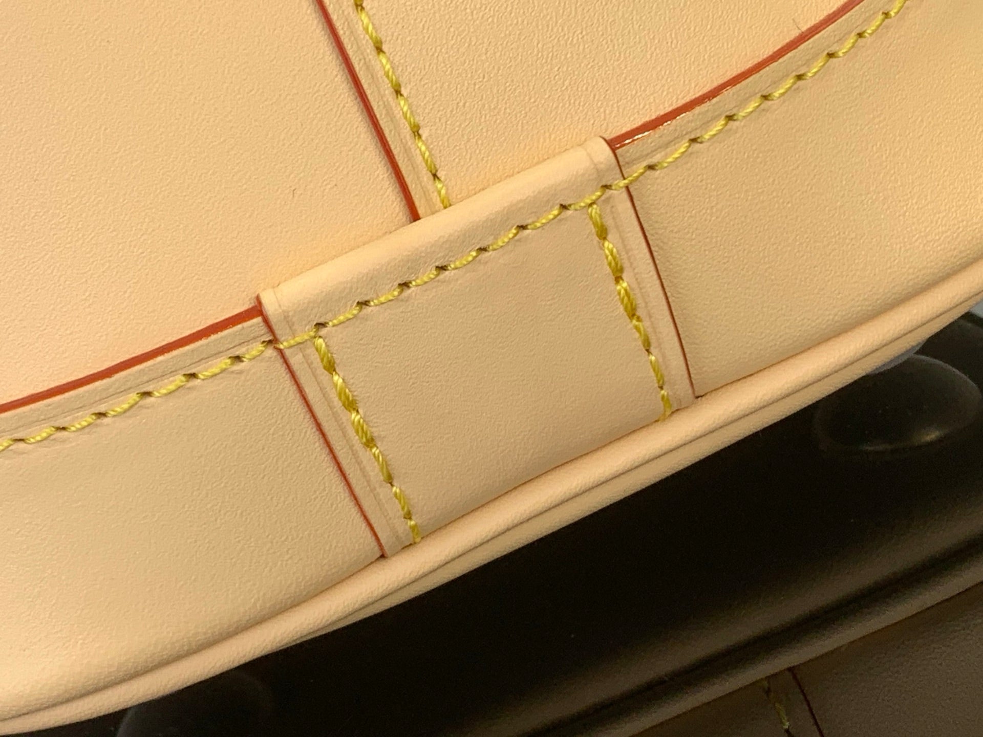 Tote bag close-up of beige leather edge, green stitching, and red lining panel