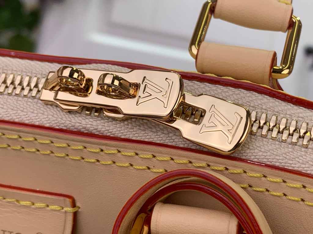 Gold zipper pull and hardware on beige tote bag with embossed logo detail