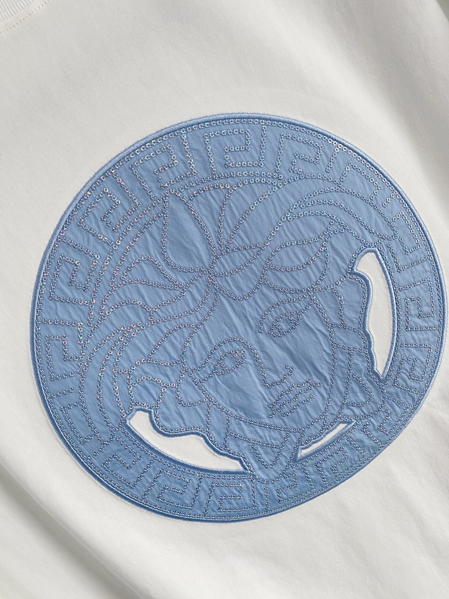 Versace T-shirt detail: large blue circular horse graphic embroidered on white.