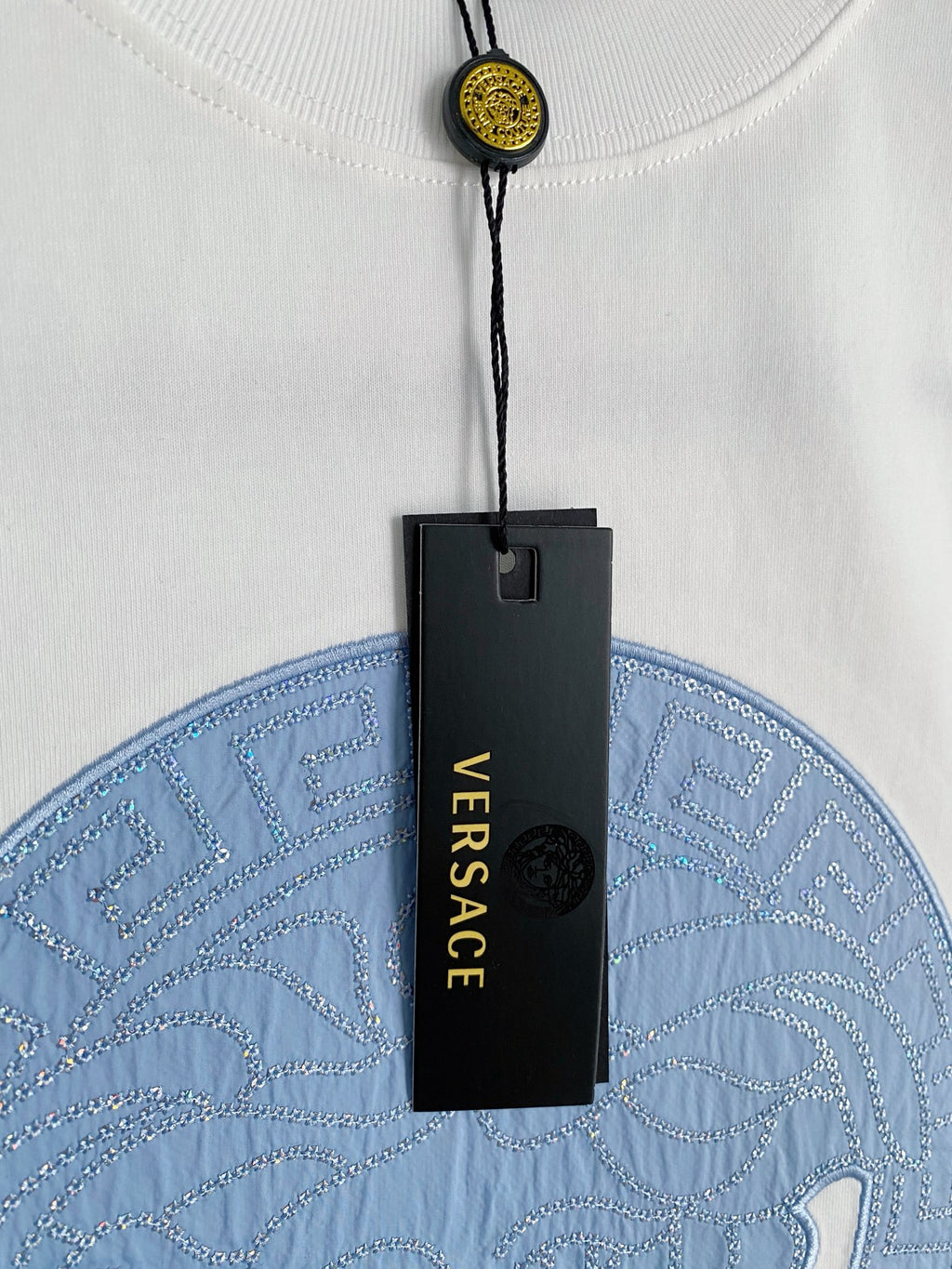 Versace T-shirt with hanging tag and blue circular horse graphic on white.