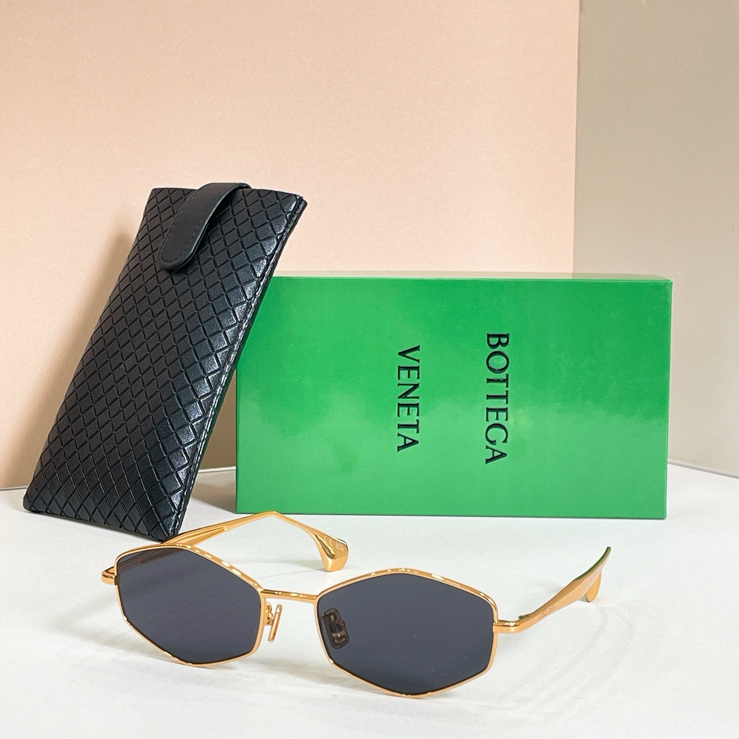 Sunglasses with dark lenses and gold-tone frames, side view with black textured case