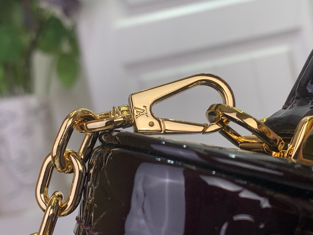 Gold clasp and chain on glossy black handbag strap
