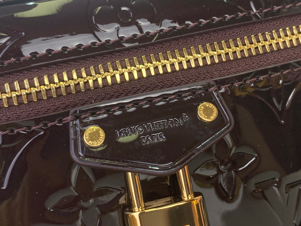 Gold zipper pull and Louis Vuitton logo plate on glossy dark leather