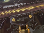 Gold zipper pull and Louis Vuitton logo plate on glossy dark leather