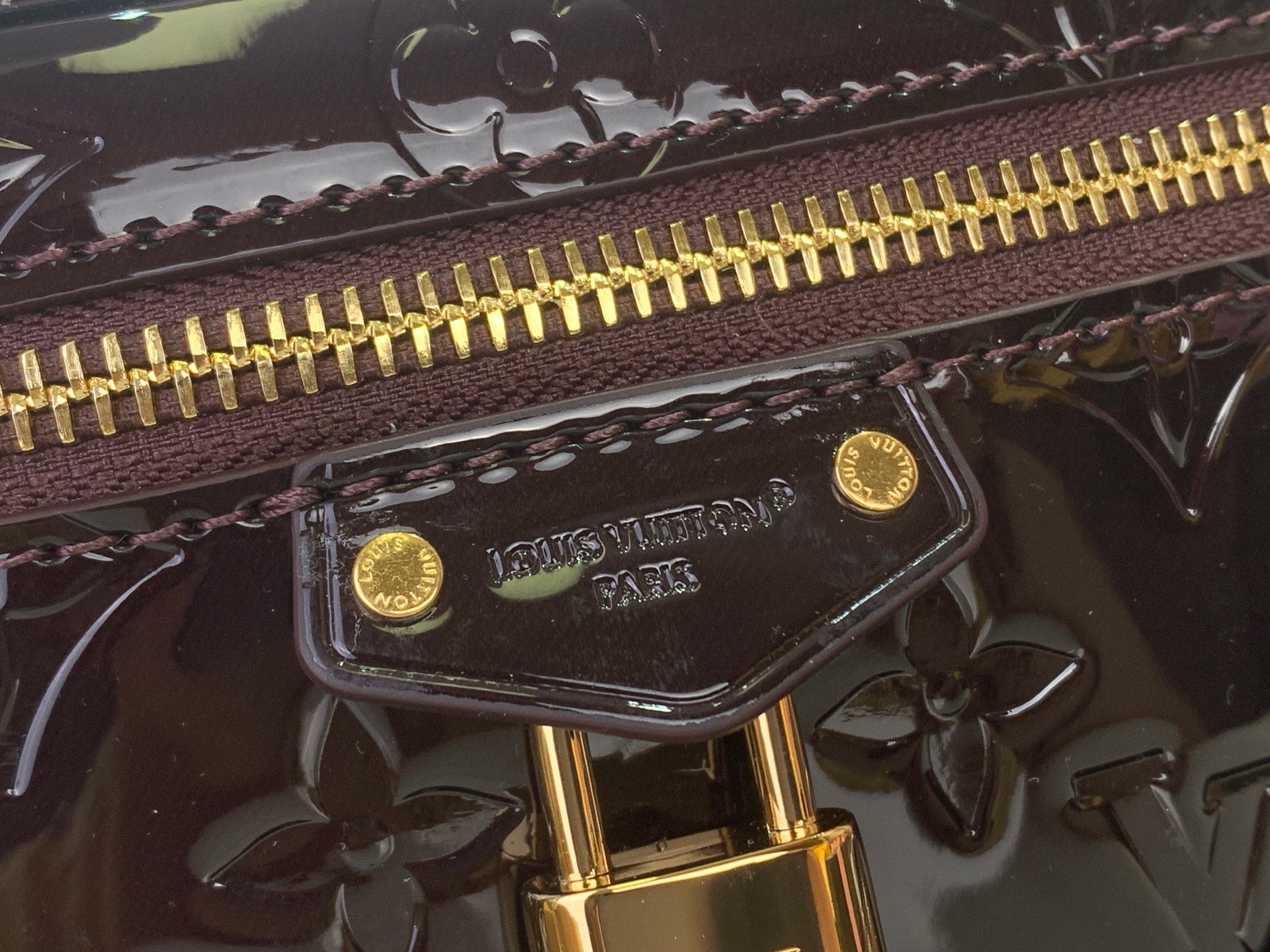 Gold zipper pull and Louis Vuitton logo plate on glossy dark leather
