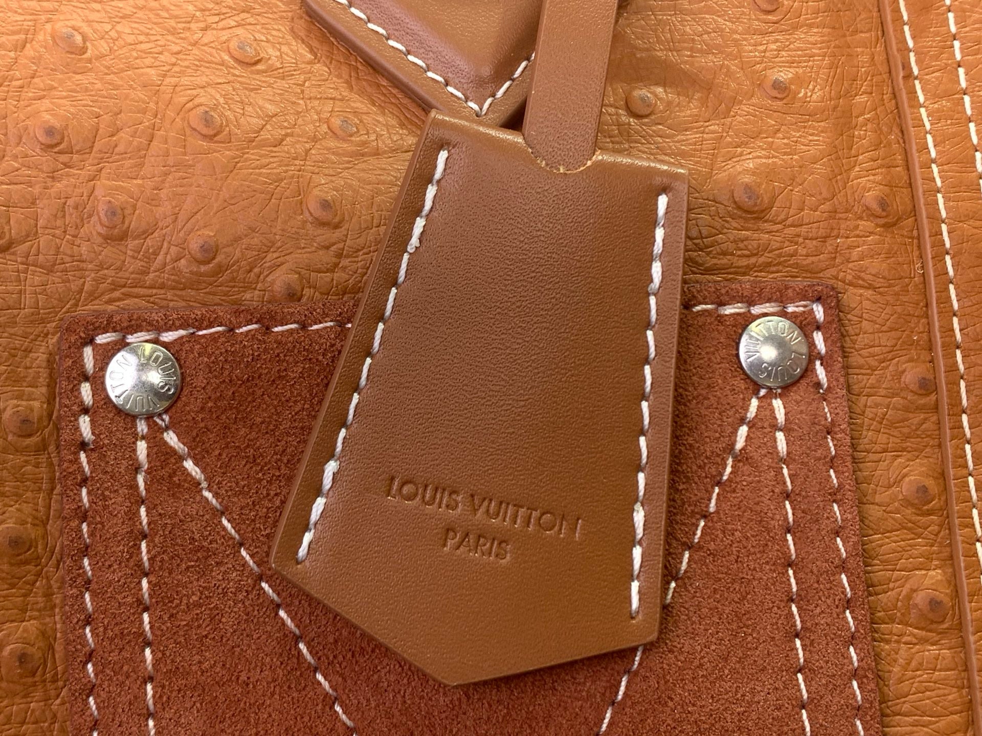 Tan leather Louis Vuitton tag with metal snaps and 'LOUIS VUITTON PARIS' engraving.
