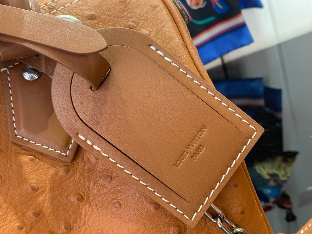 Tan leather Louis Vuitton luggage tag with stitched edge and metal snap.