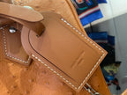 Close-up of tan leather bag charm with Louis Vuitton PARIS stamped on a small tag