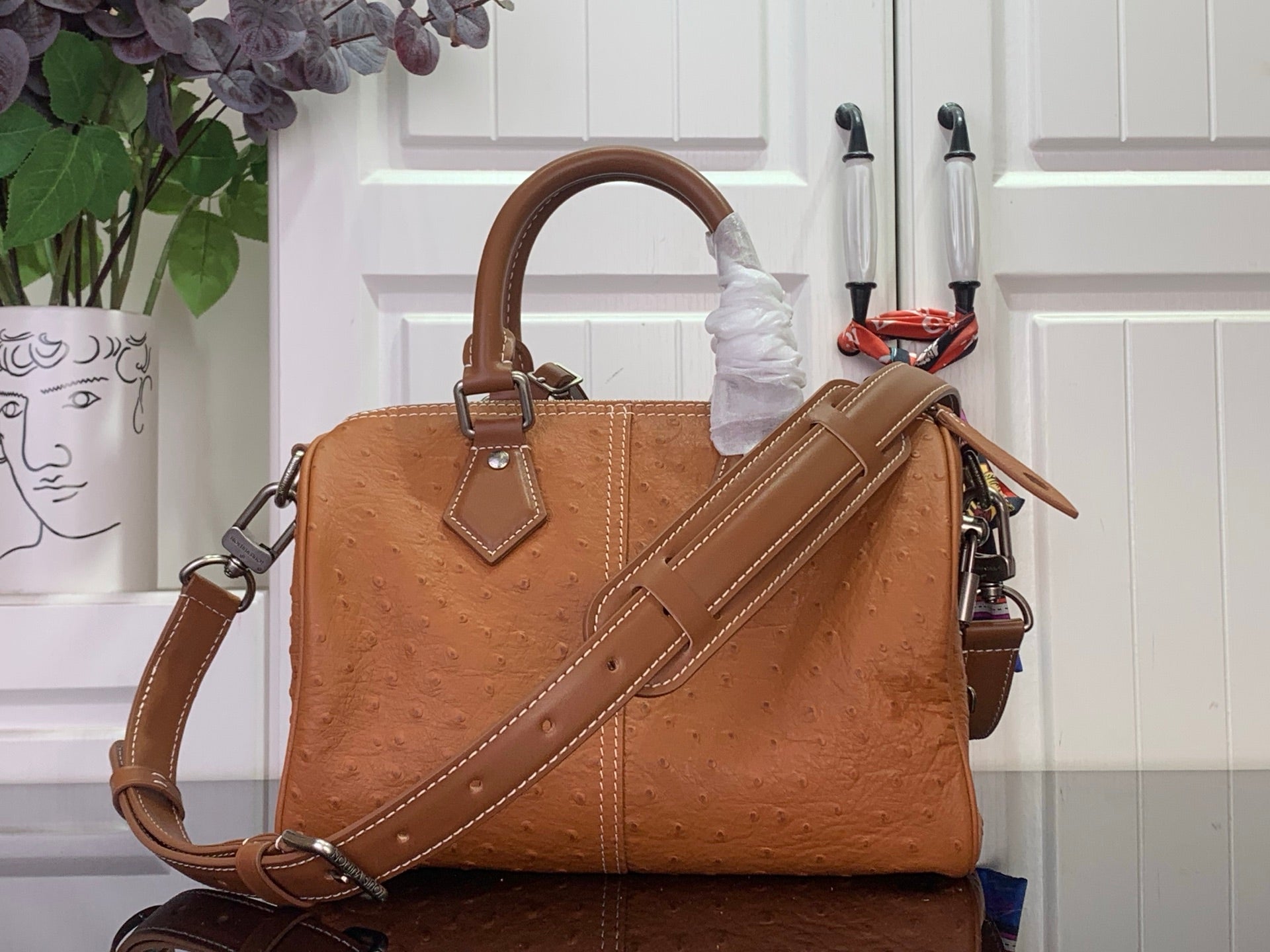 Tan leather handbag with top handle and wide crossbody strap, front logo tag detail